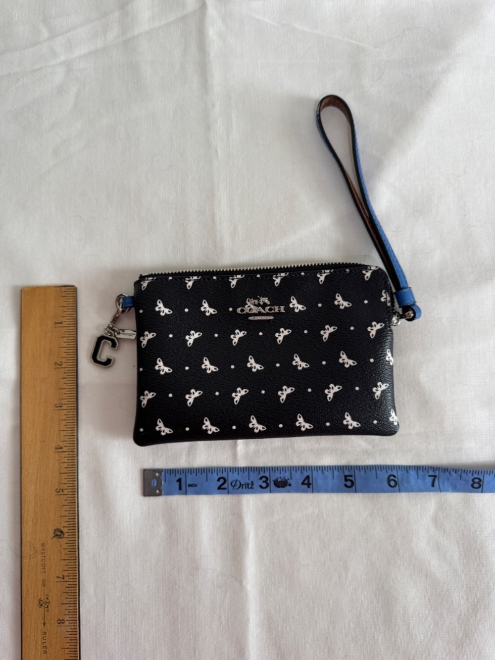 Black Coach wristlet with white butterfly print and black C varsity charm